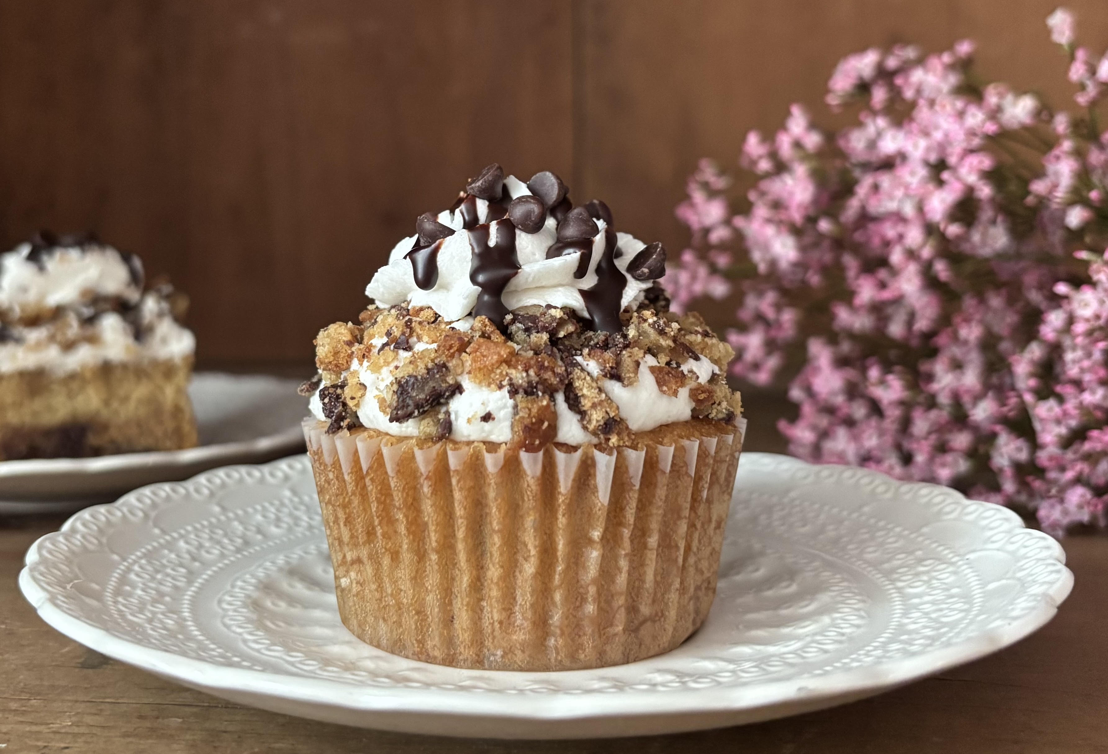 A vegan cupcake with whipped frosting, cookie crumble and chocolate drizzle on a white plate